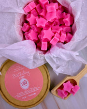 Pink star-shaped wax melts in a container labeled 'Birthday Cake' with a wooden scoop.