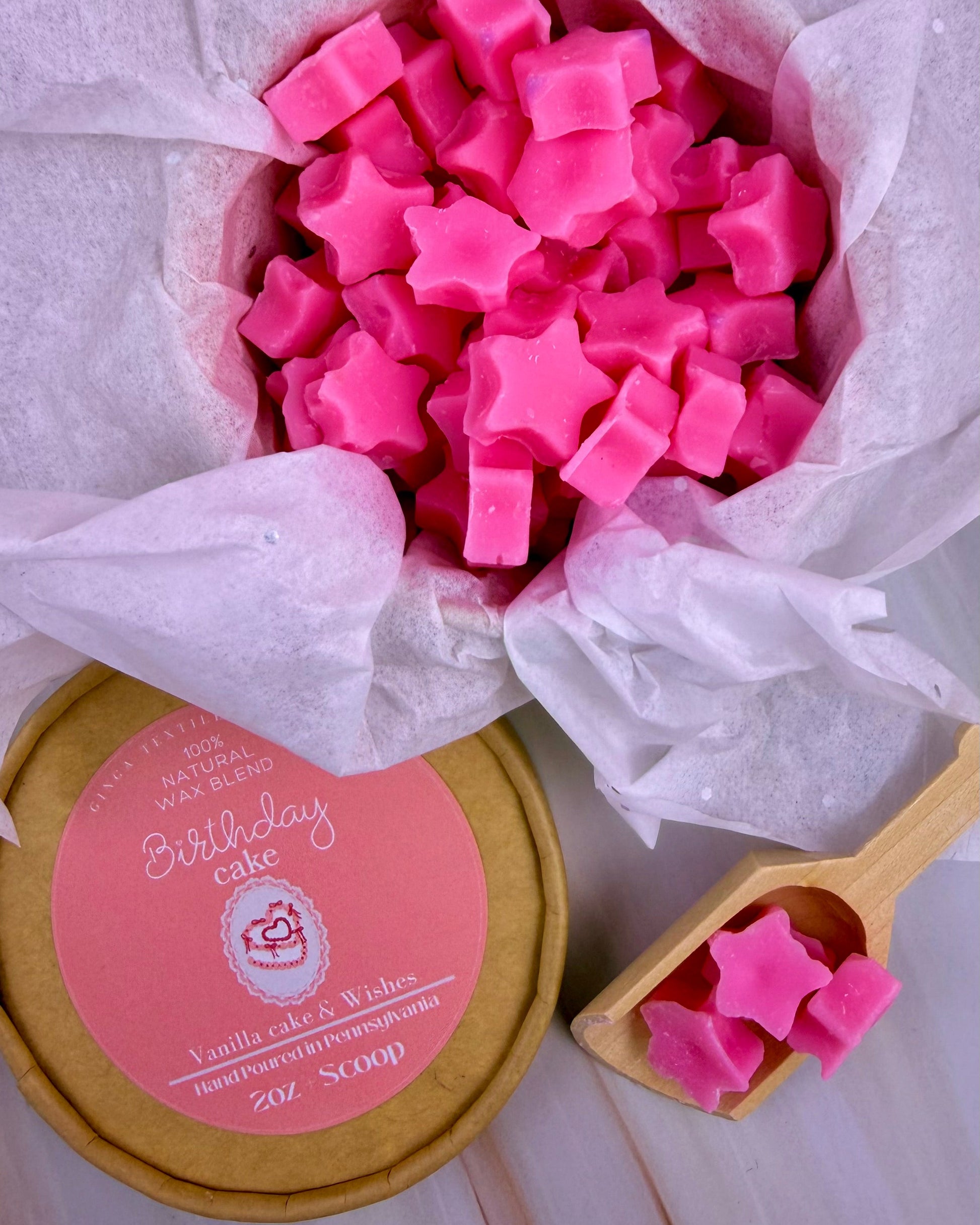 Pink star-shaped wax melts in a container labeled 'Birthday Cake' with a wooden scoop.