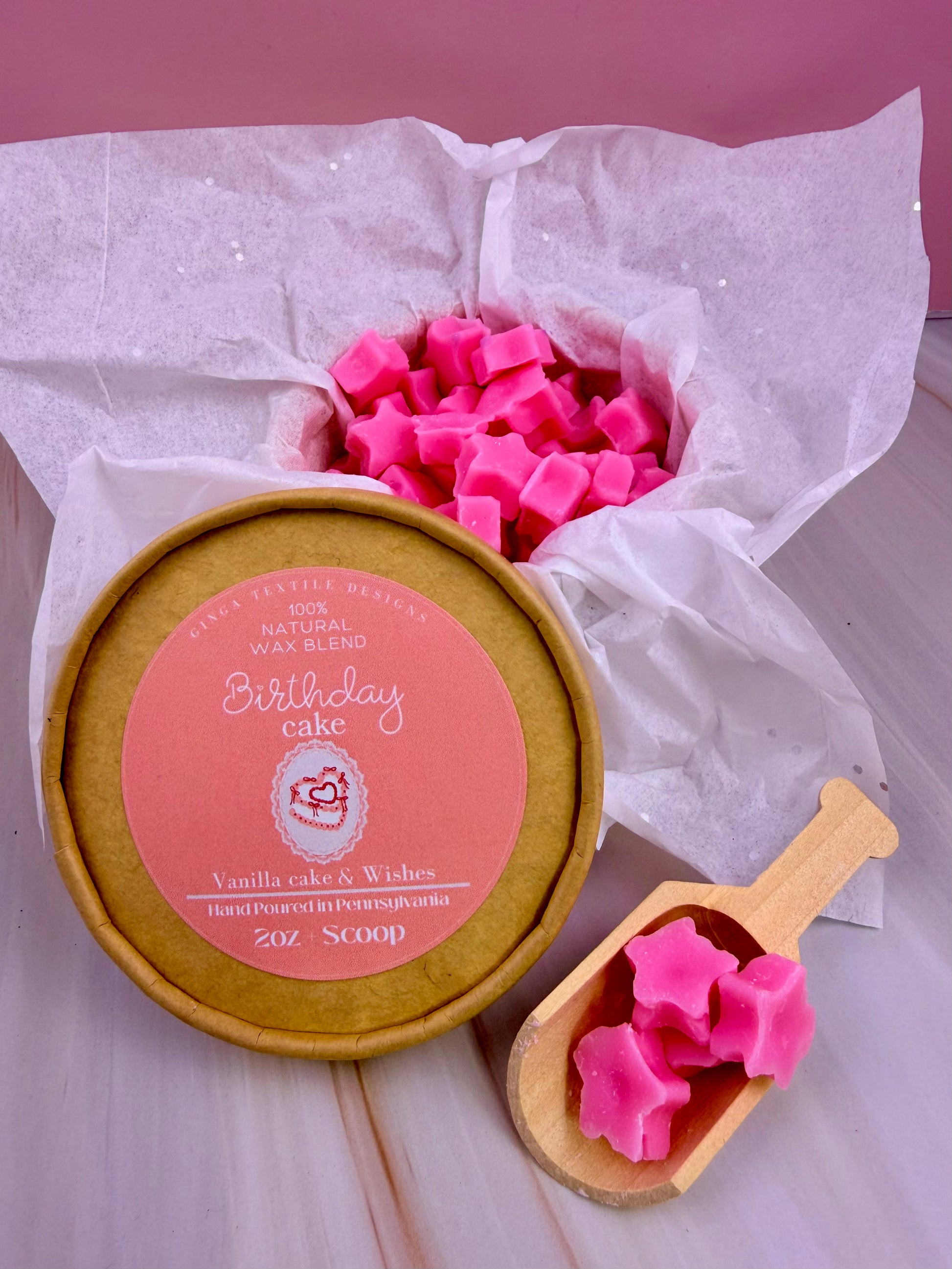 Pink wax melts in a wooden scoop and container on white tissue paper with a pink background