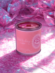 Pink candle in a can labeled 'Birthday Cake' on a pink and white textured background