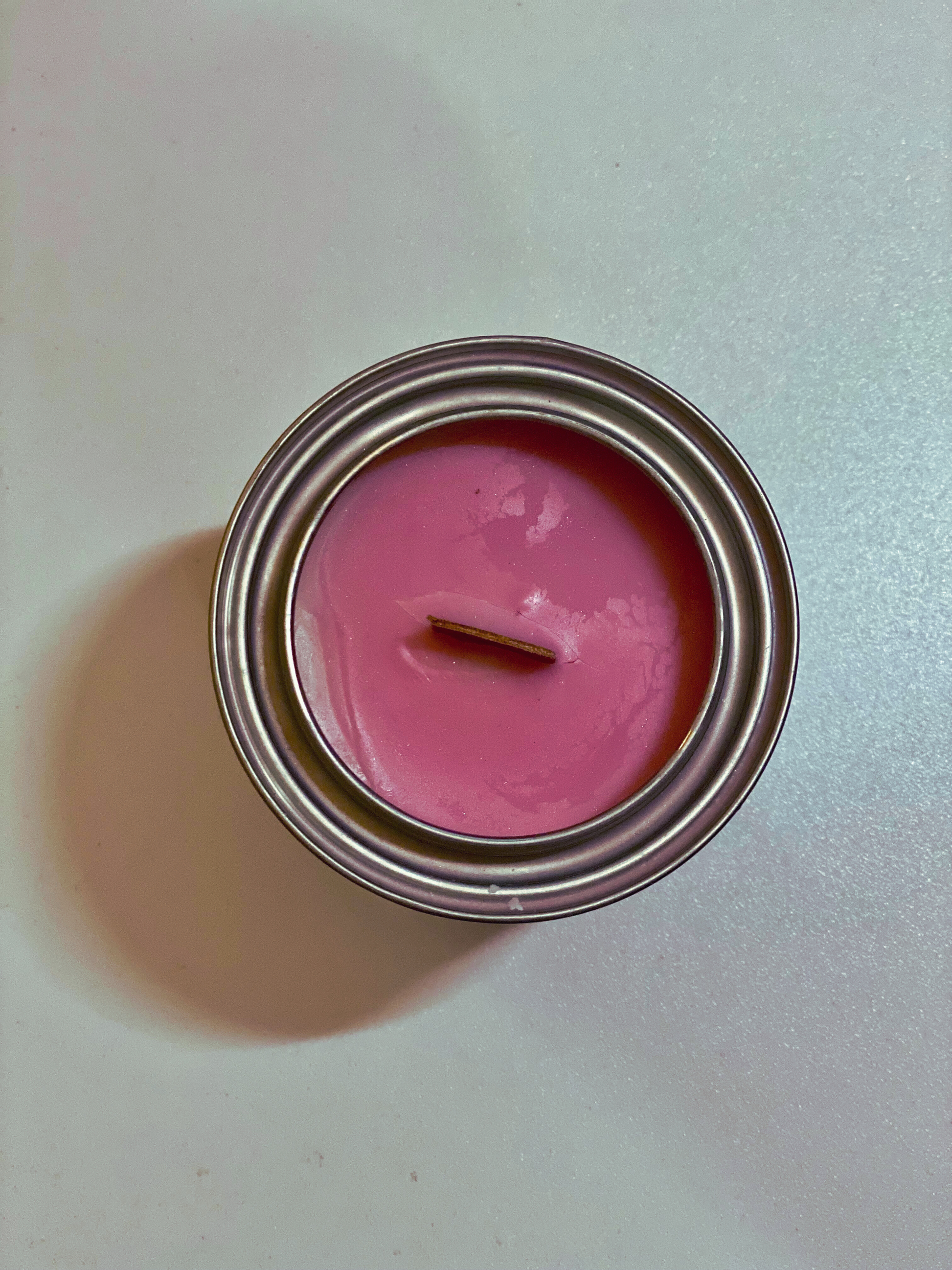 point of view from above of a pink candle in a metal container on a light gray background