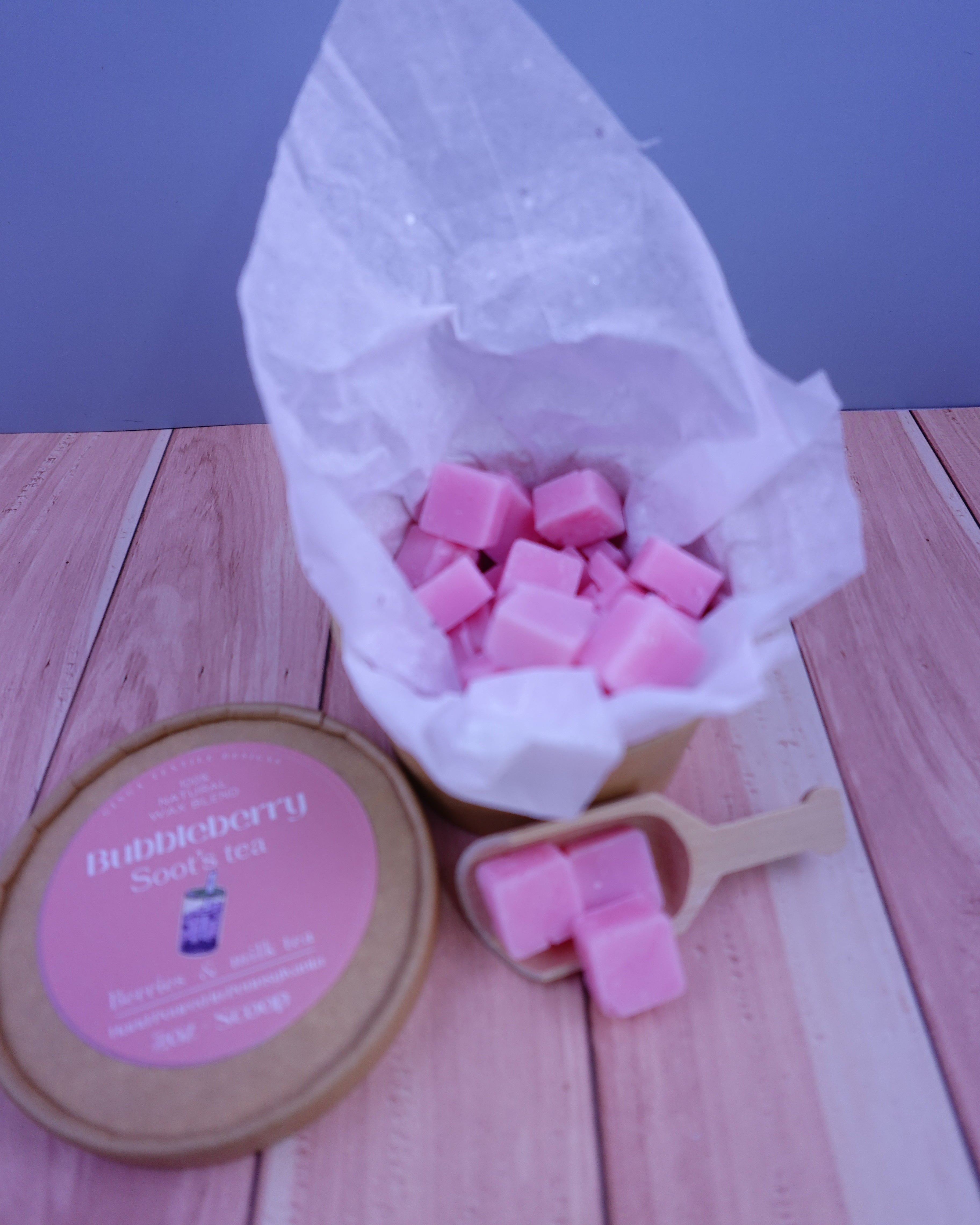 Pink wax cubes in a white bag on a wooden surface with a pink container.