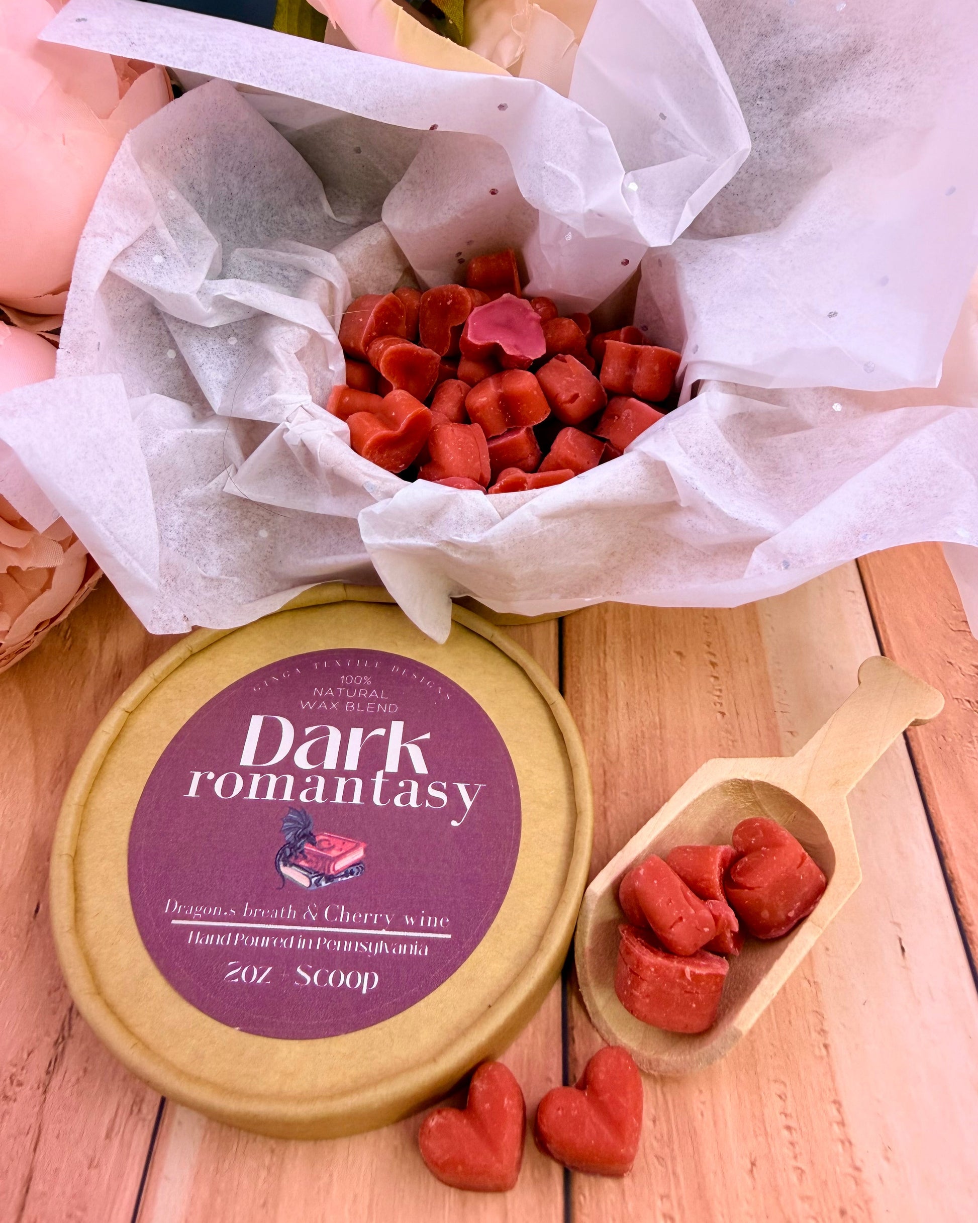 Heart shaped wax melts in the scent Dark Romantasy on a light-colored wood table with white tissue paper and flowers in the background