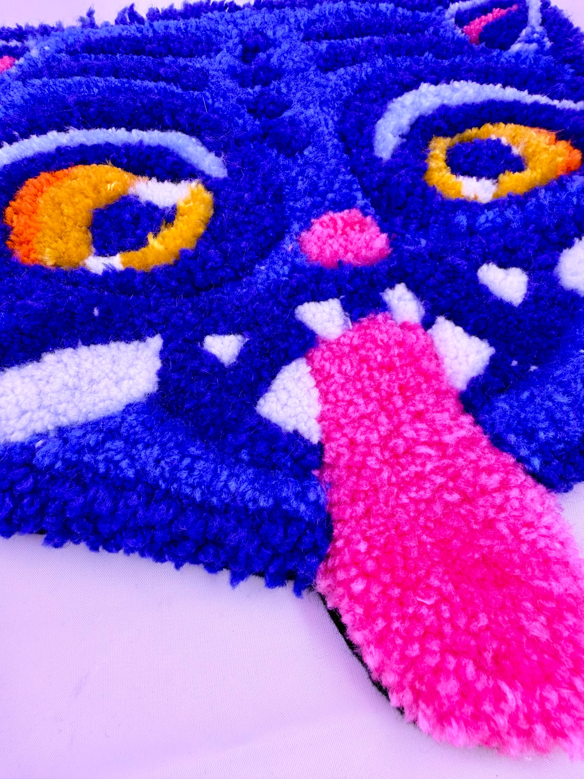 Close-up of a colorful tufted rug with blue, pink, and yellow details on a white background.
