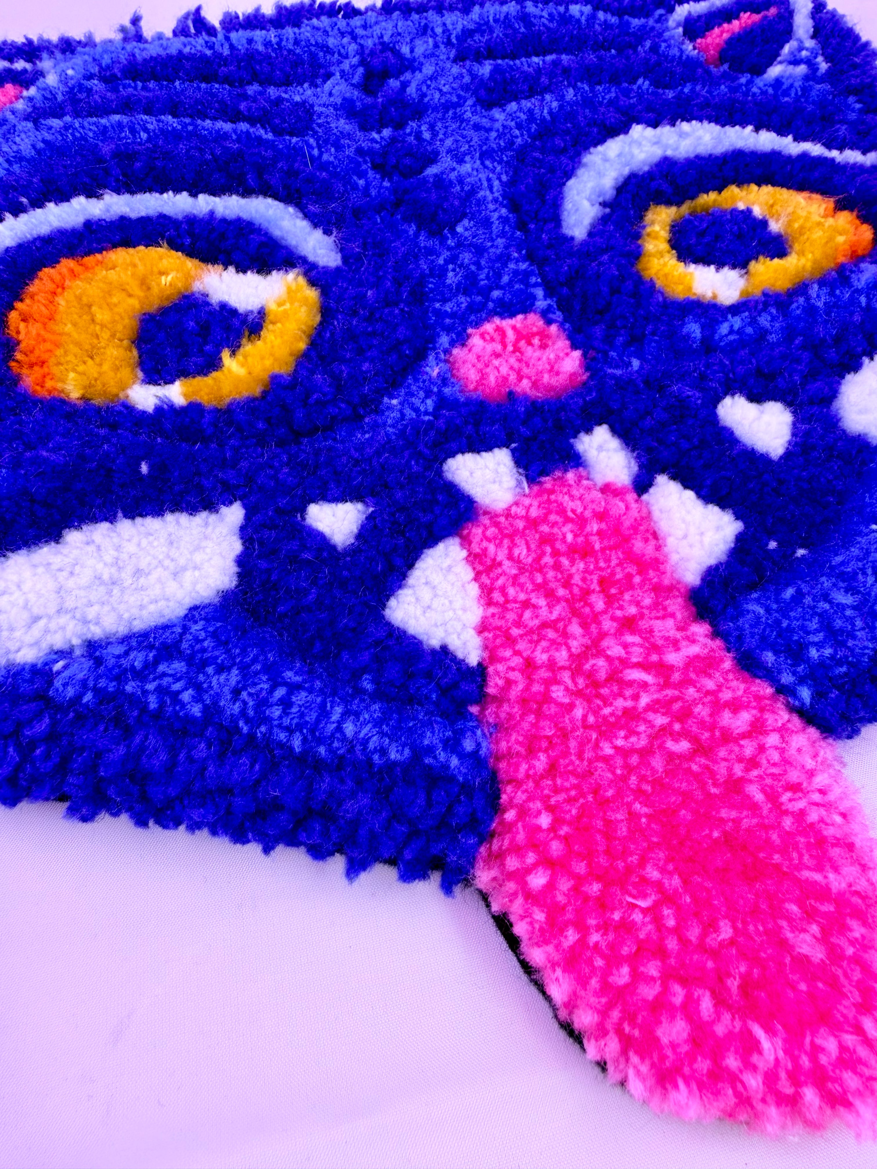 Close-up of a colorful tufted rug with blue, pink, and yellow details on a white background.