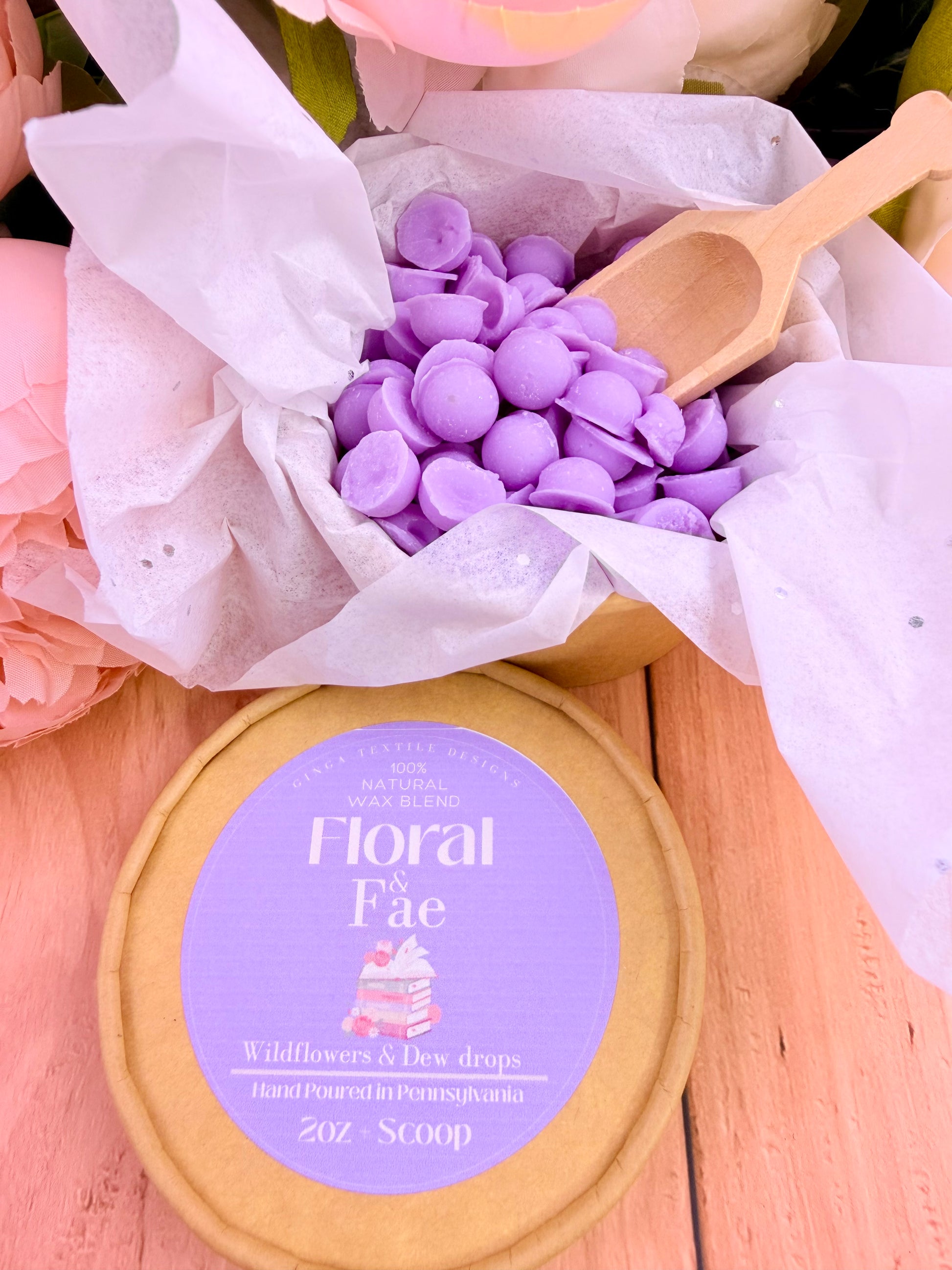 Container of purple floral Fae wax melts with a wooden scoop on a wooden surface.