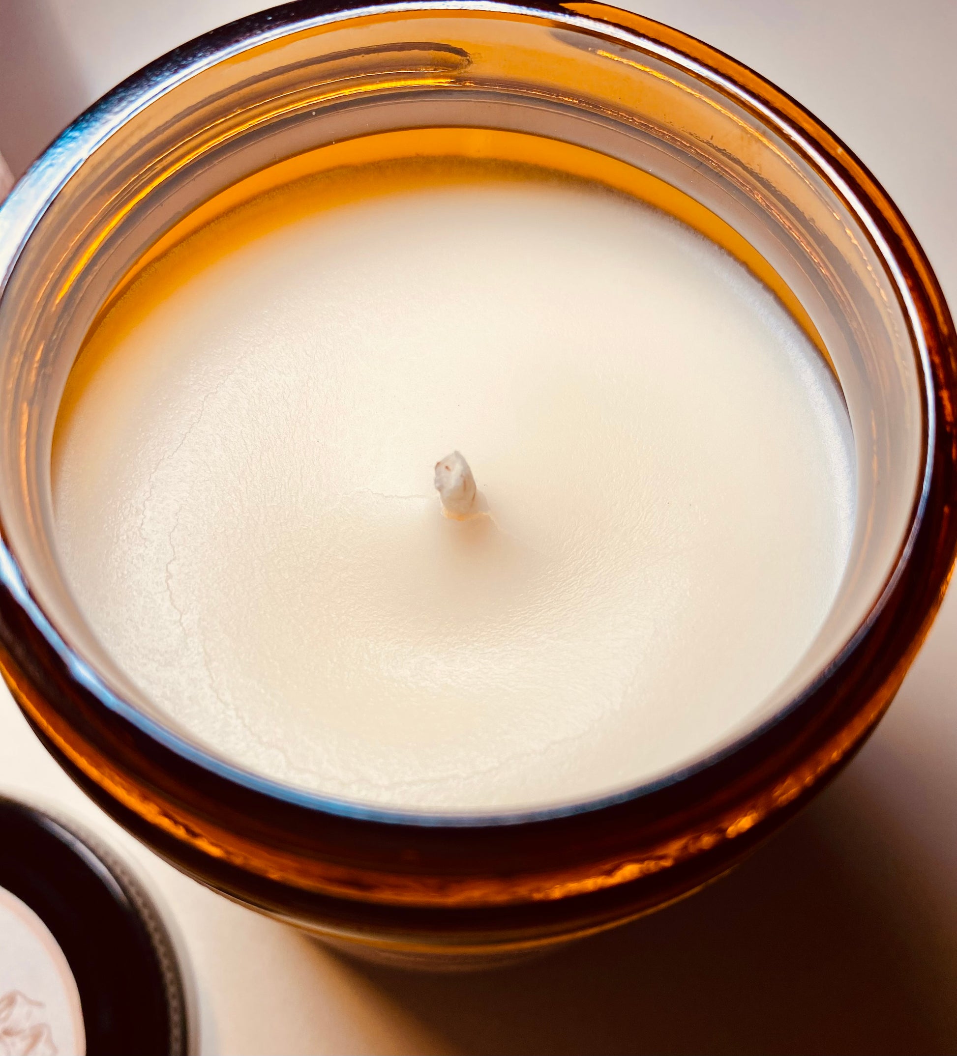 Close-up of a white candle in an amber glass jar on a neutral background