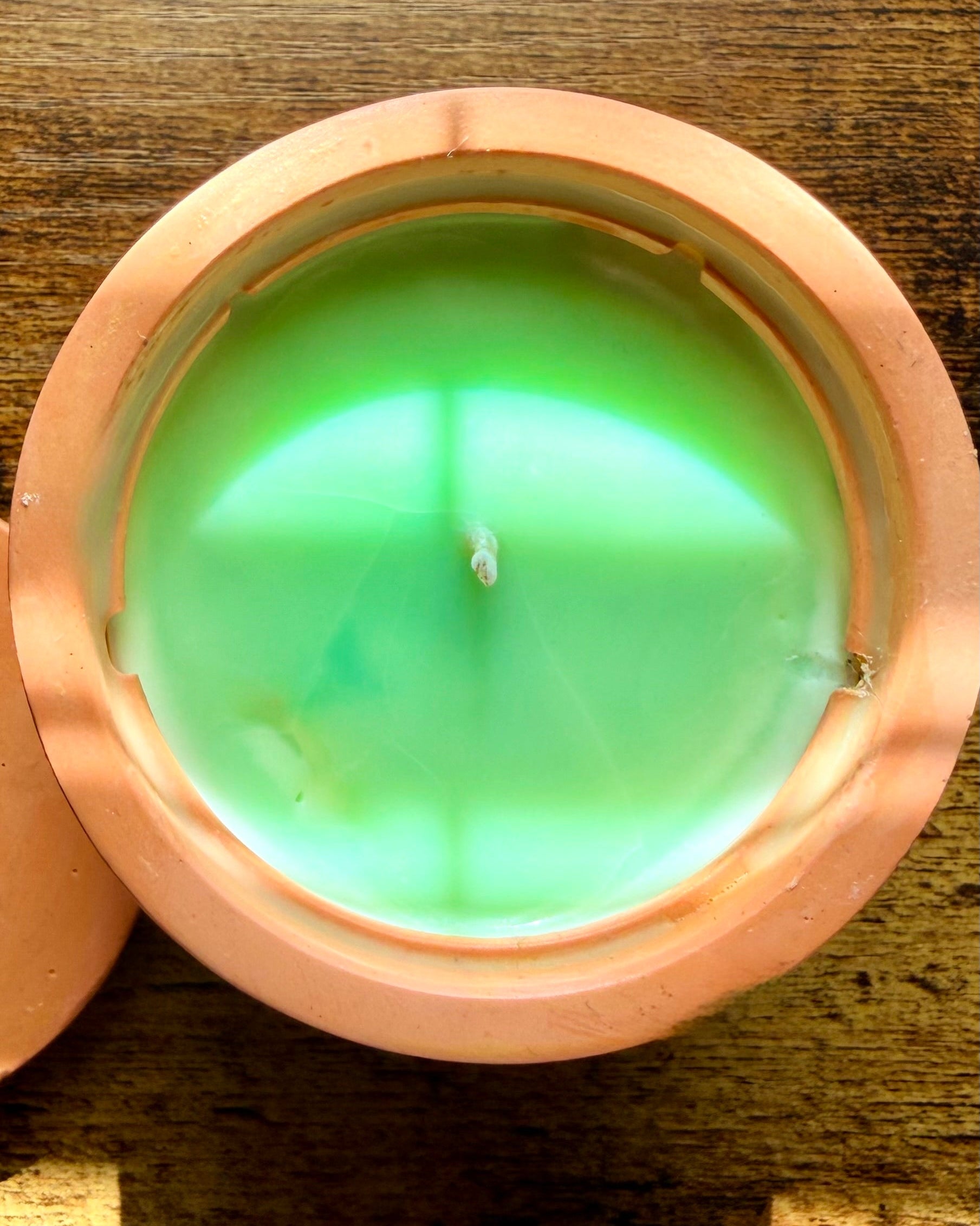 Green candle in a terracotta holder on a wooden surface