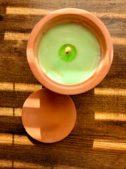 Green candle in a terracotta holder on a wooden surface