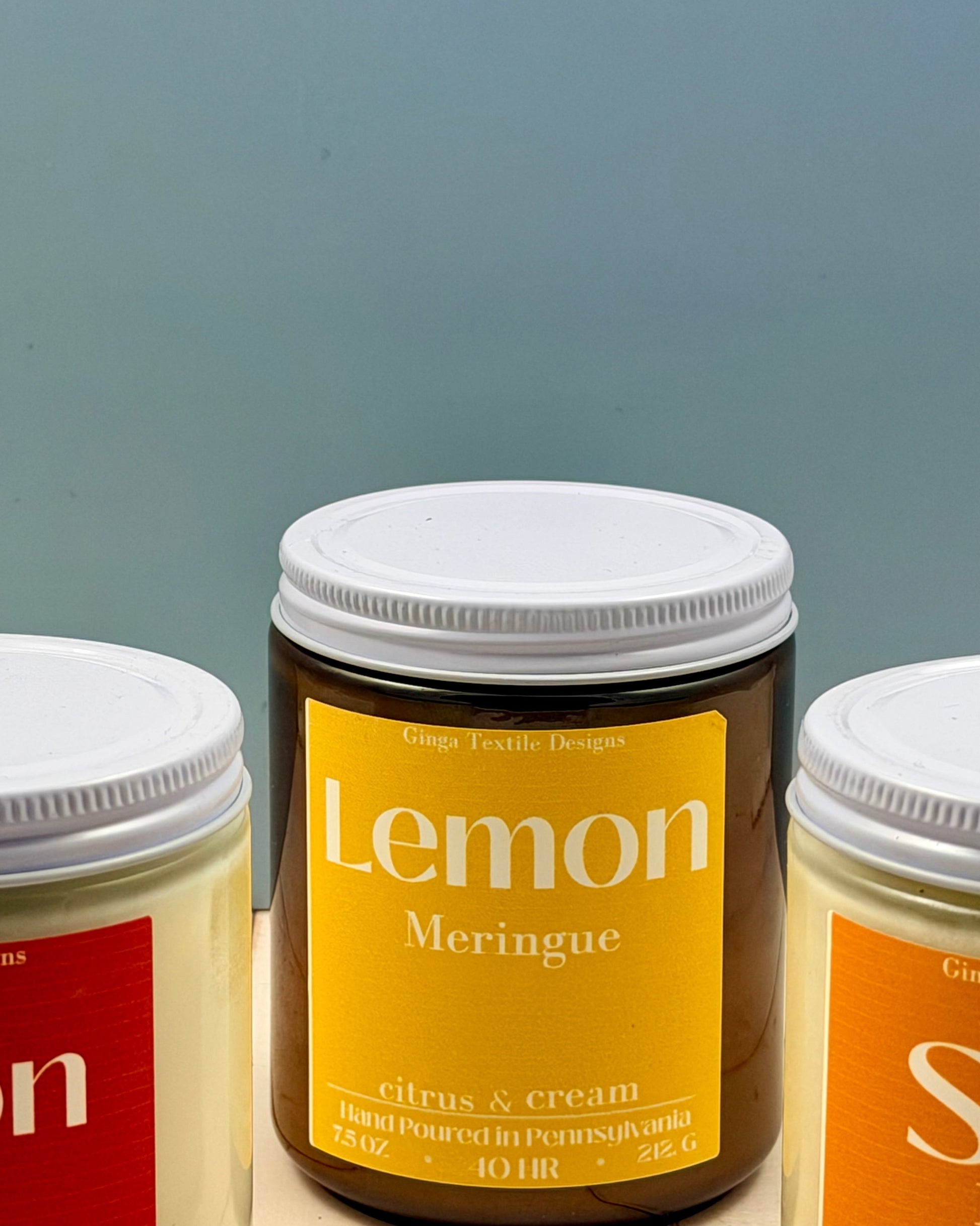 Three jars of 'Lemon Meringue' with different colored labels on a gray background