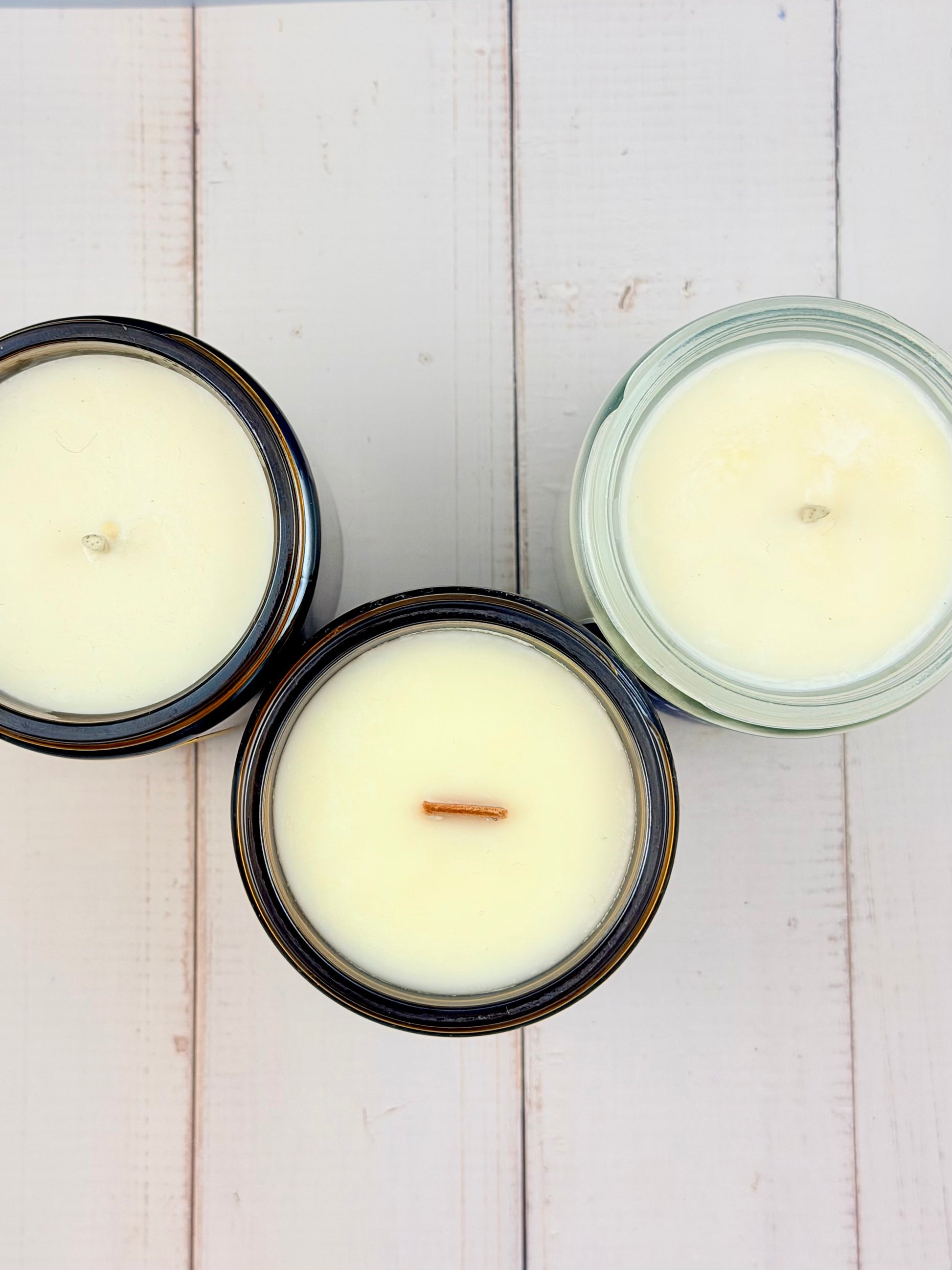 Three candles in glass jars on a light wooden surface
