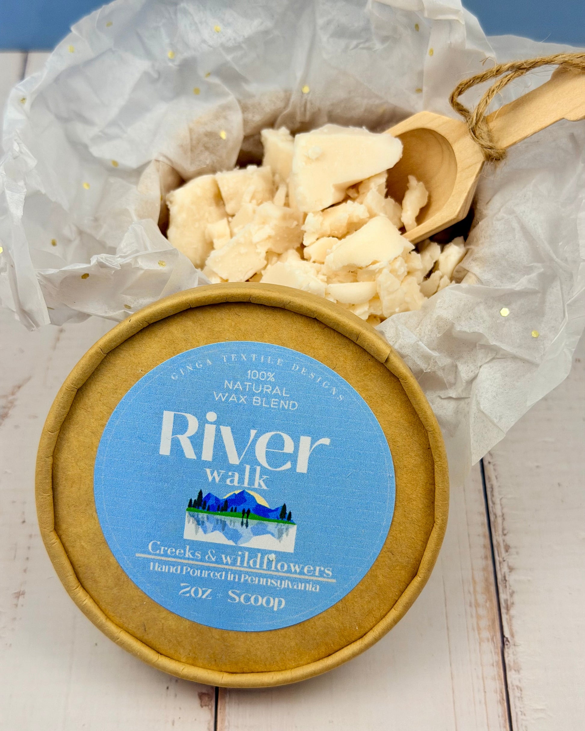 Container of River Walk wax blend with a wooden scoop on a light wooden surface.