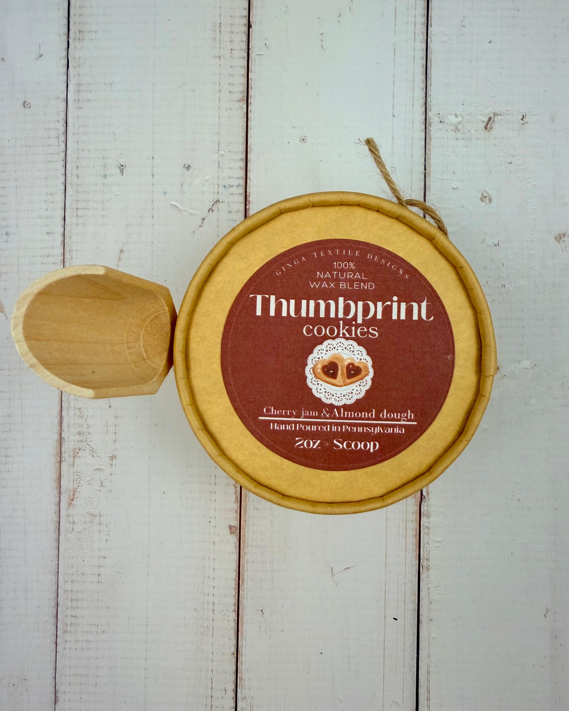 Closed container of Thumbprint cookies wax melts with a wooden scoop on a wooden surface
