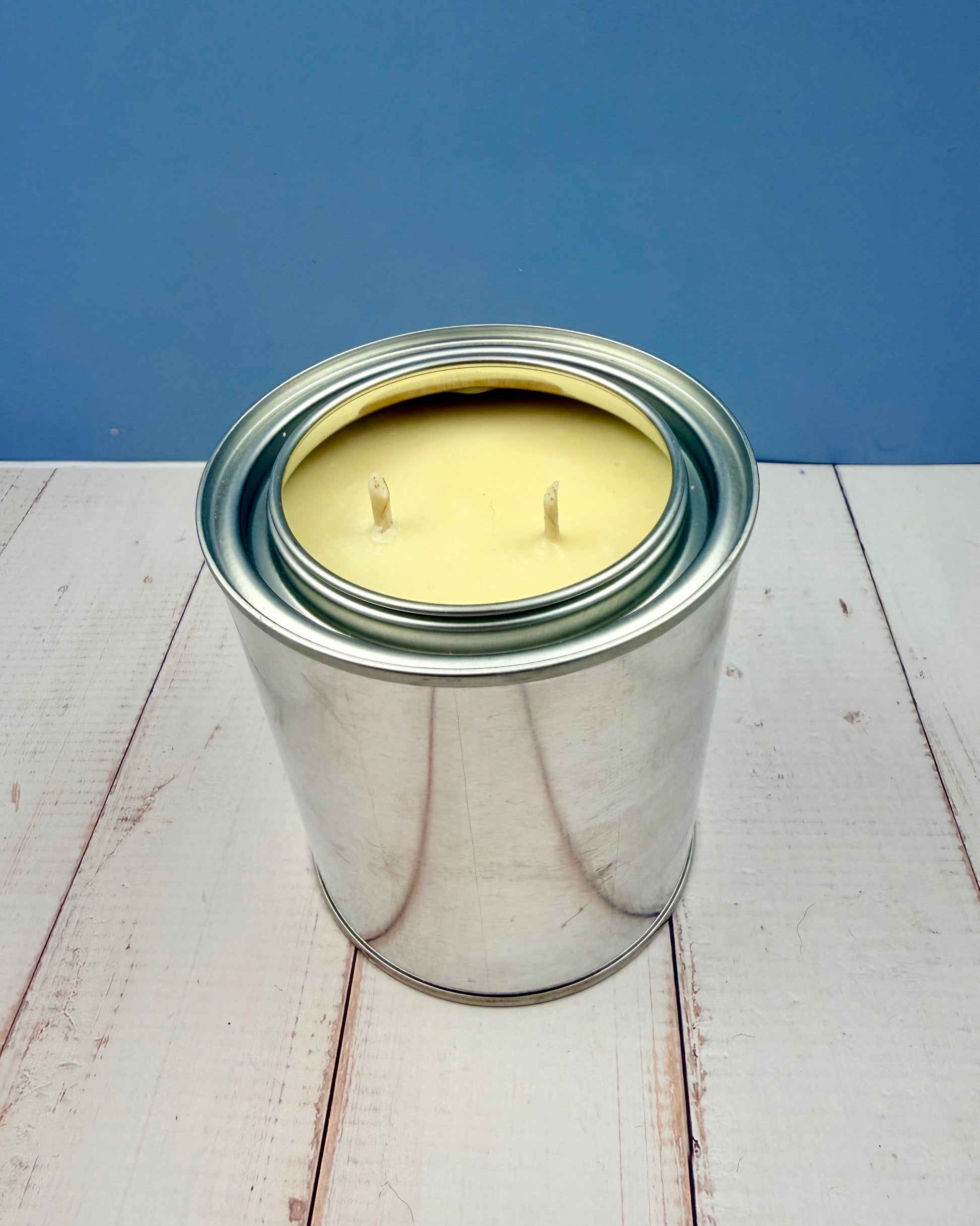 Metal paint can with a candle inside on a wooden surface and blue background