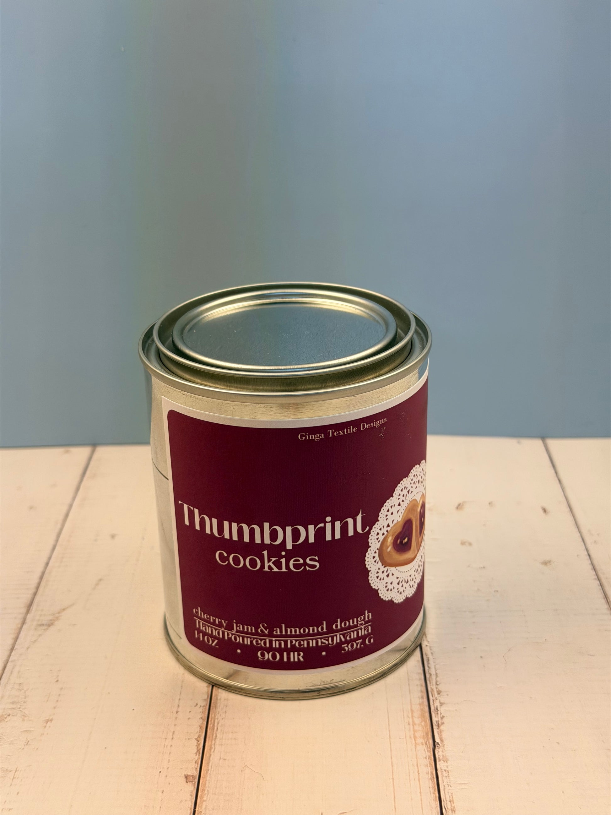 Can of Thumbprint Cookies scented candle on a wooden surface with a light gray background