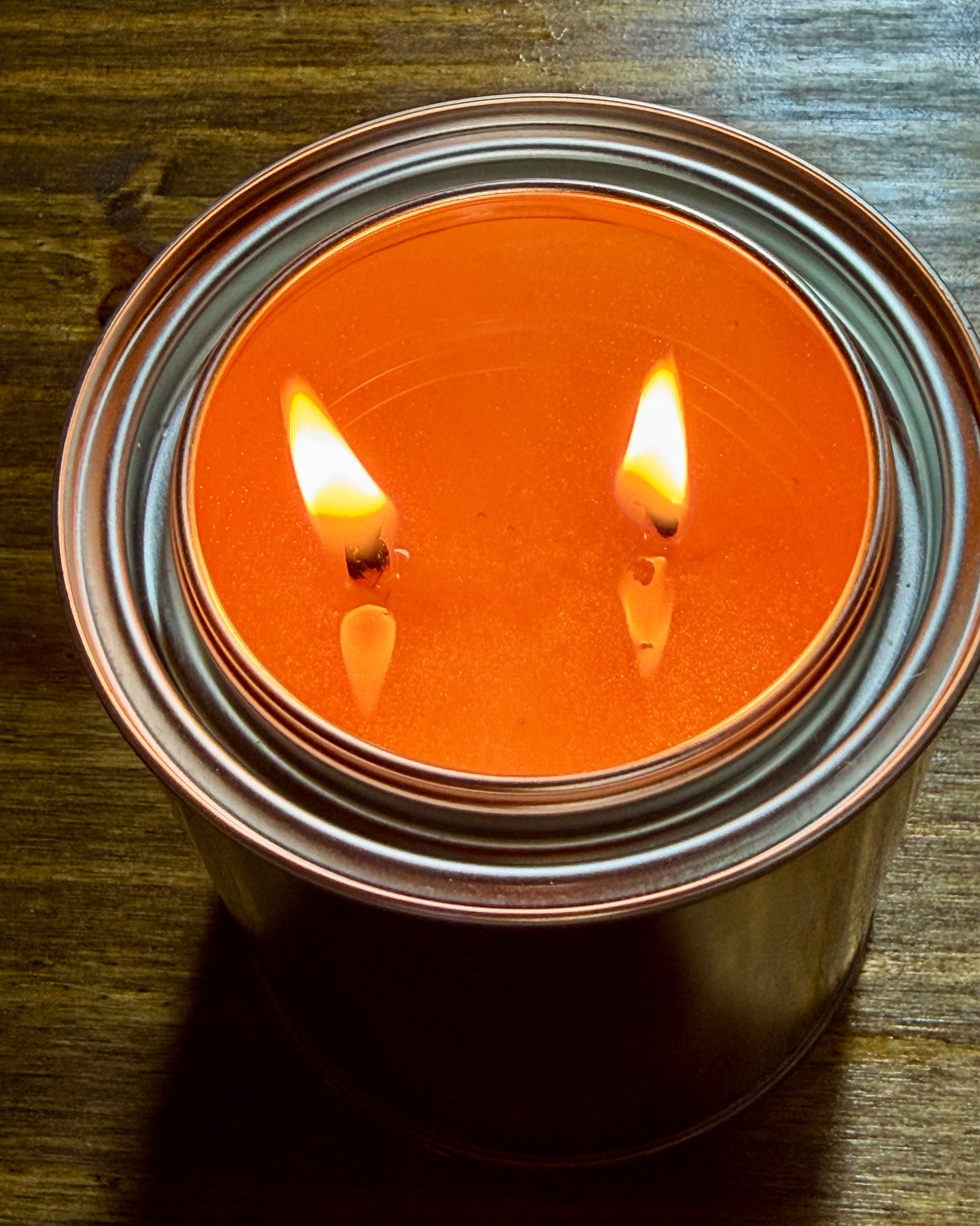 Candle in a metal container with two flames on a wooden surface