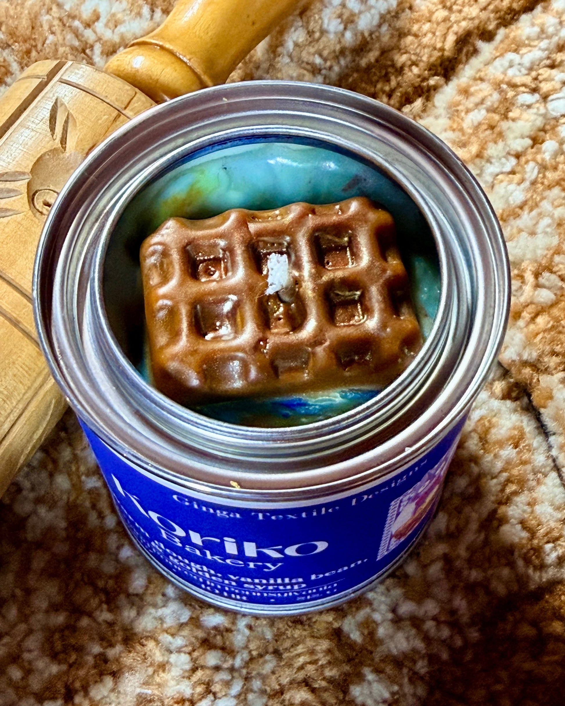 Can of Koriko Bakery Candle with a waffle wax embed inside, on a textured surface.