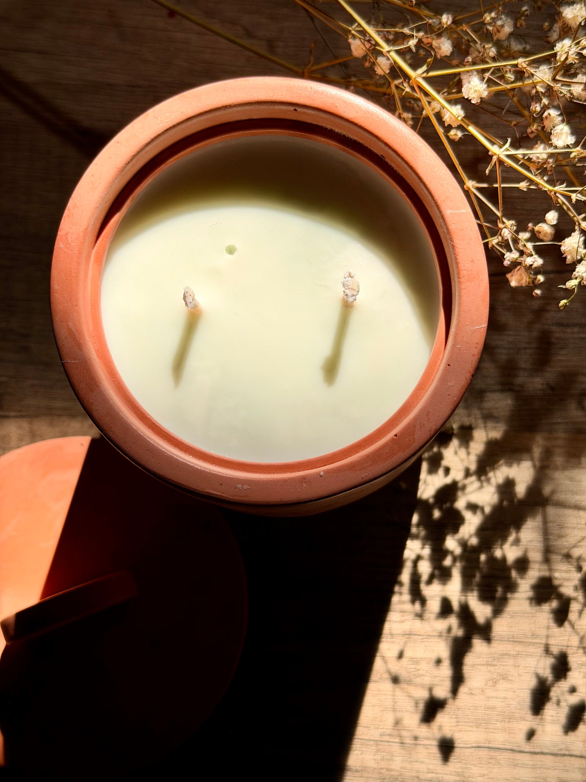 Candle in a terracotta container on a wooden surface with dried flowers.