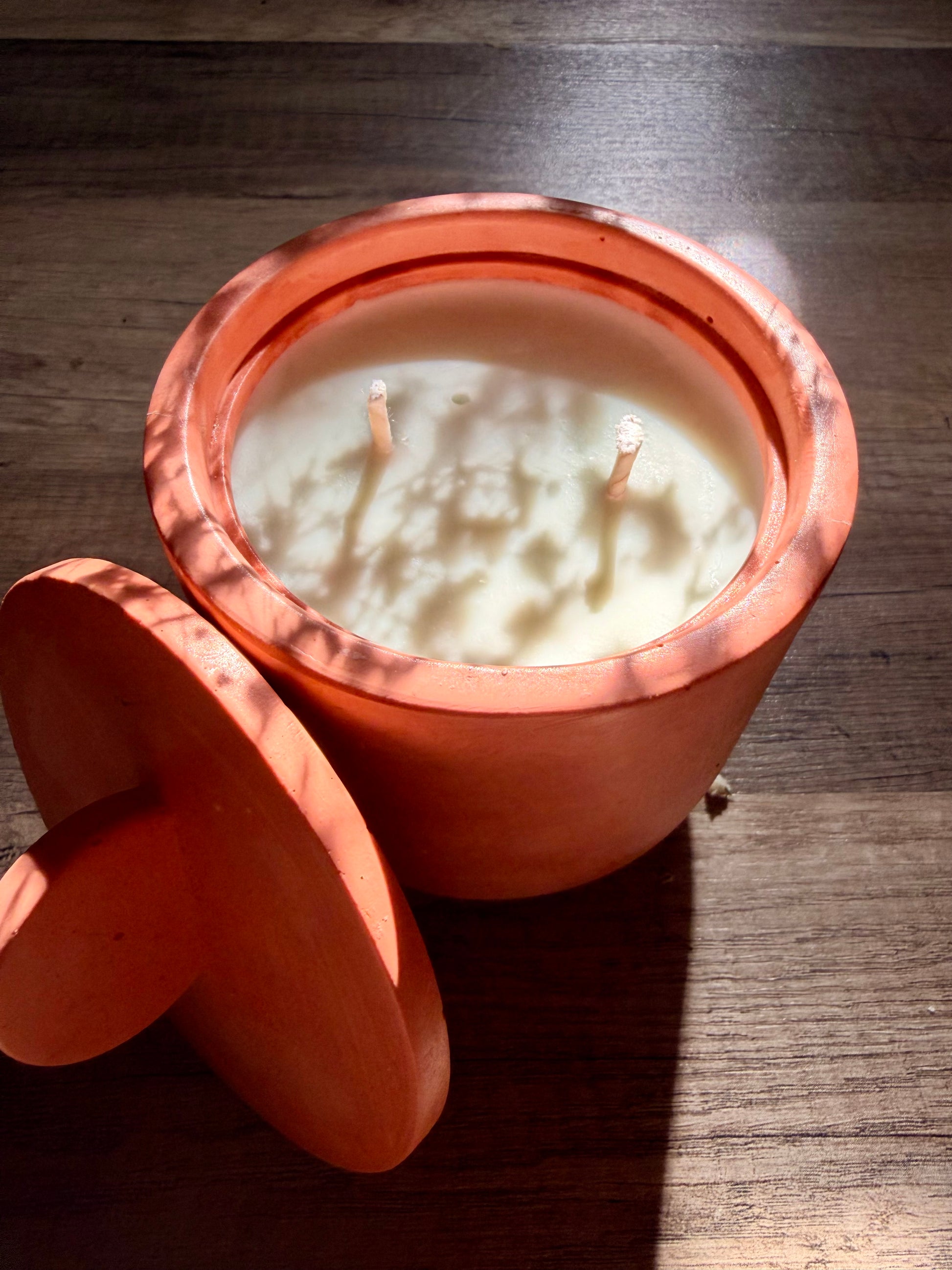 Candle in a terracotta pot with a circle lid on a wooden surface