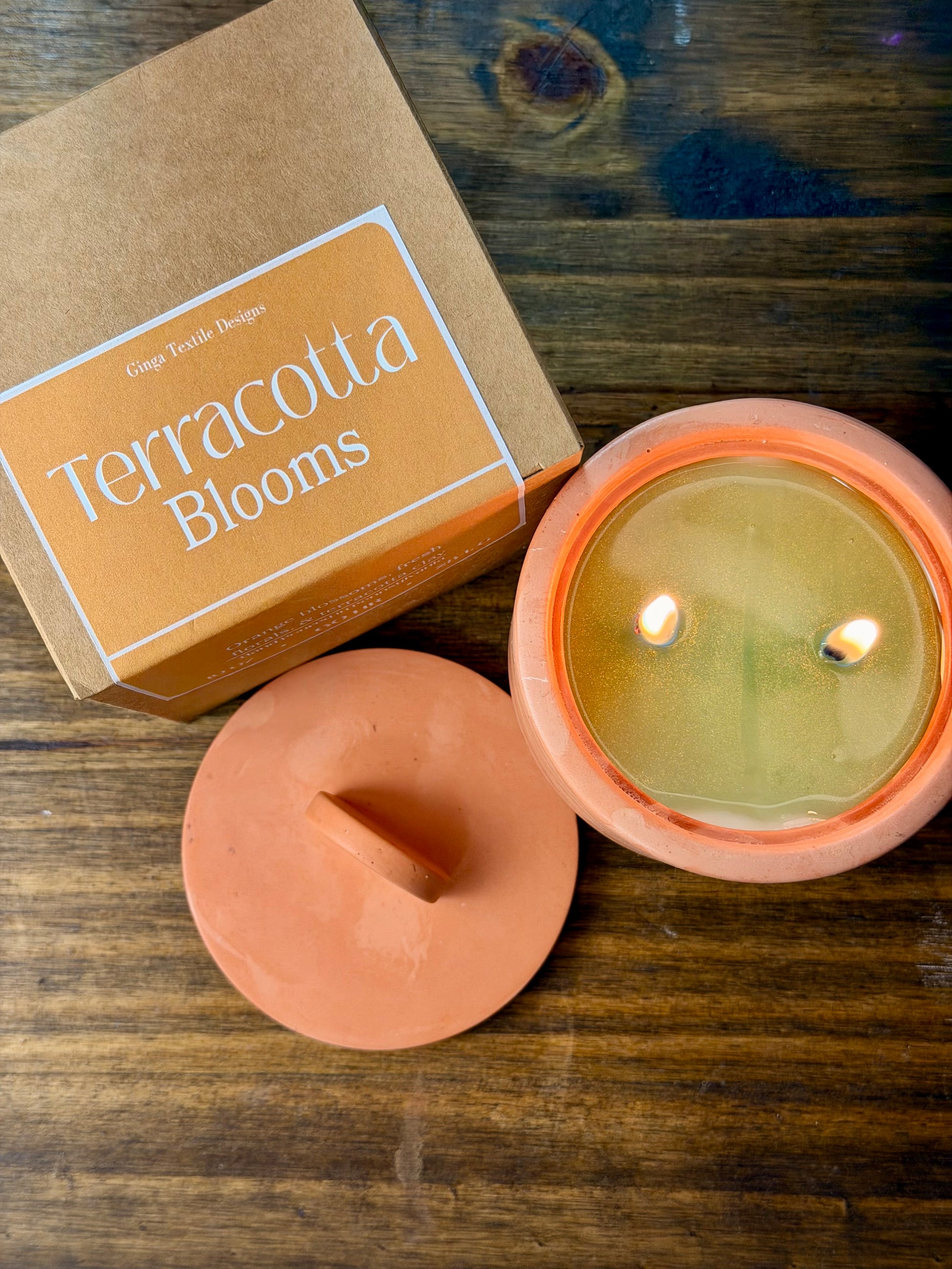 Terracotta candle with lid and packaging labeled 'Terracotta Blooms' on a wooden surface.