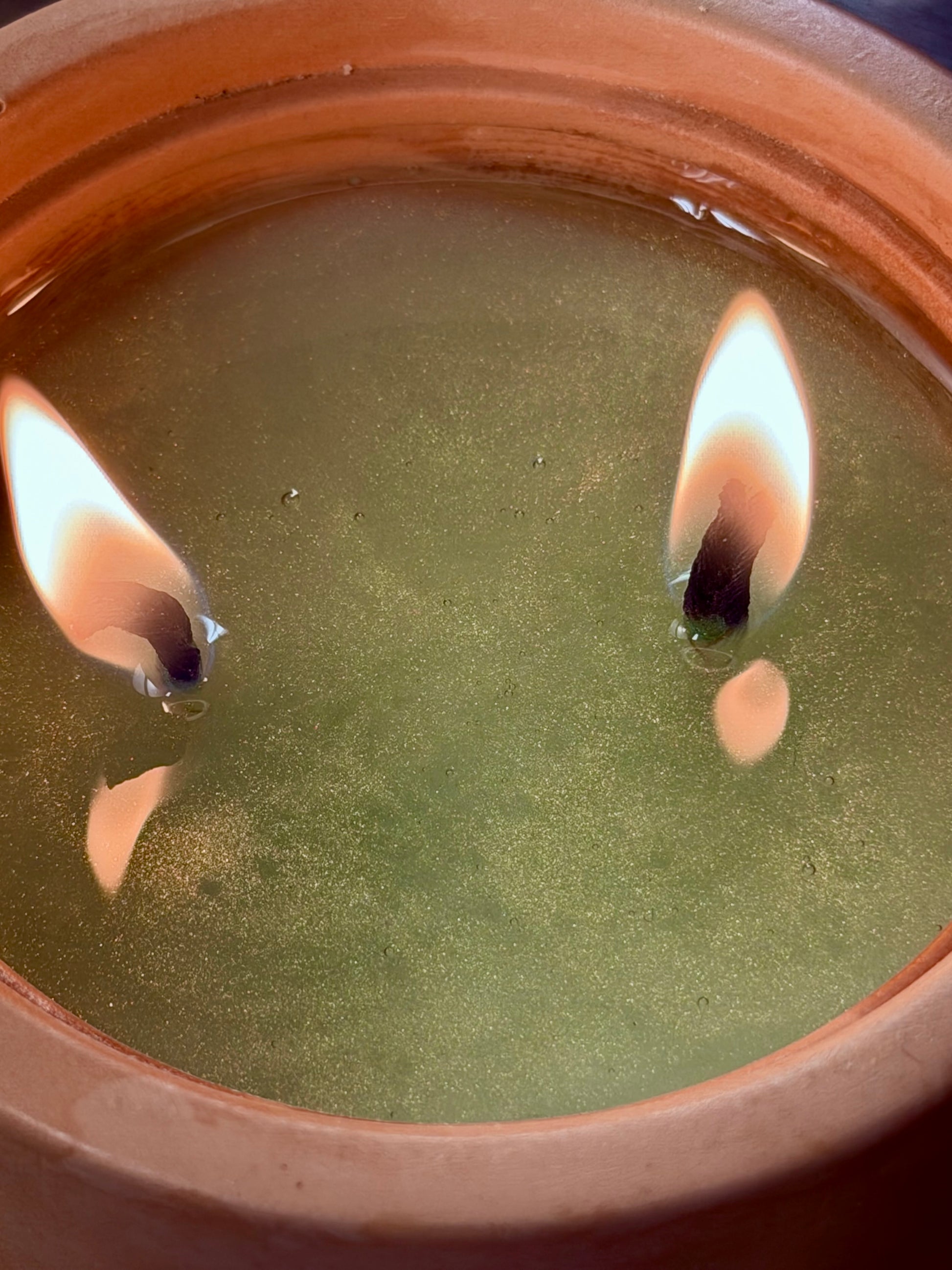 Close-up of a candle with wicks floating in wax inside a terracotta pot.
