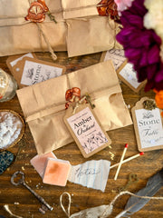 A styled flat-lay of vintage-themed paper envelopes and labels on a rustic wooden table, with wax seals, keys, matches, notes, and flowers around them.