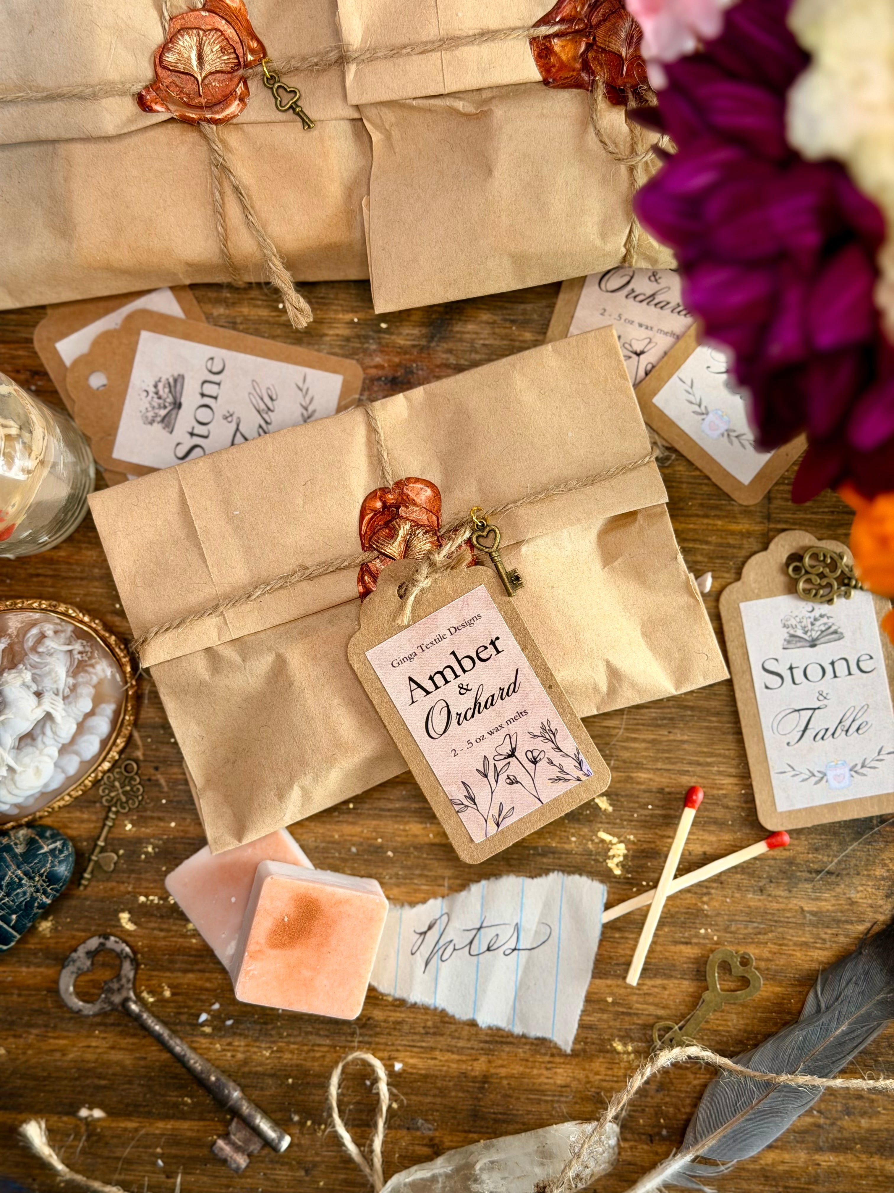 A styled flat-lay of vintage-themed paper envelopes and labels on a rustic wooden table, with wax seals, keys, matches, notes, and flowers around them.