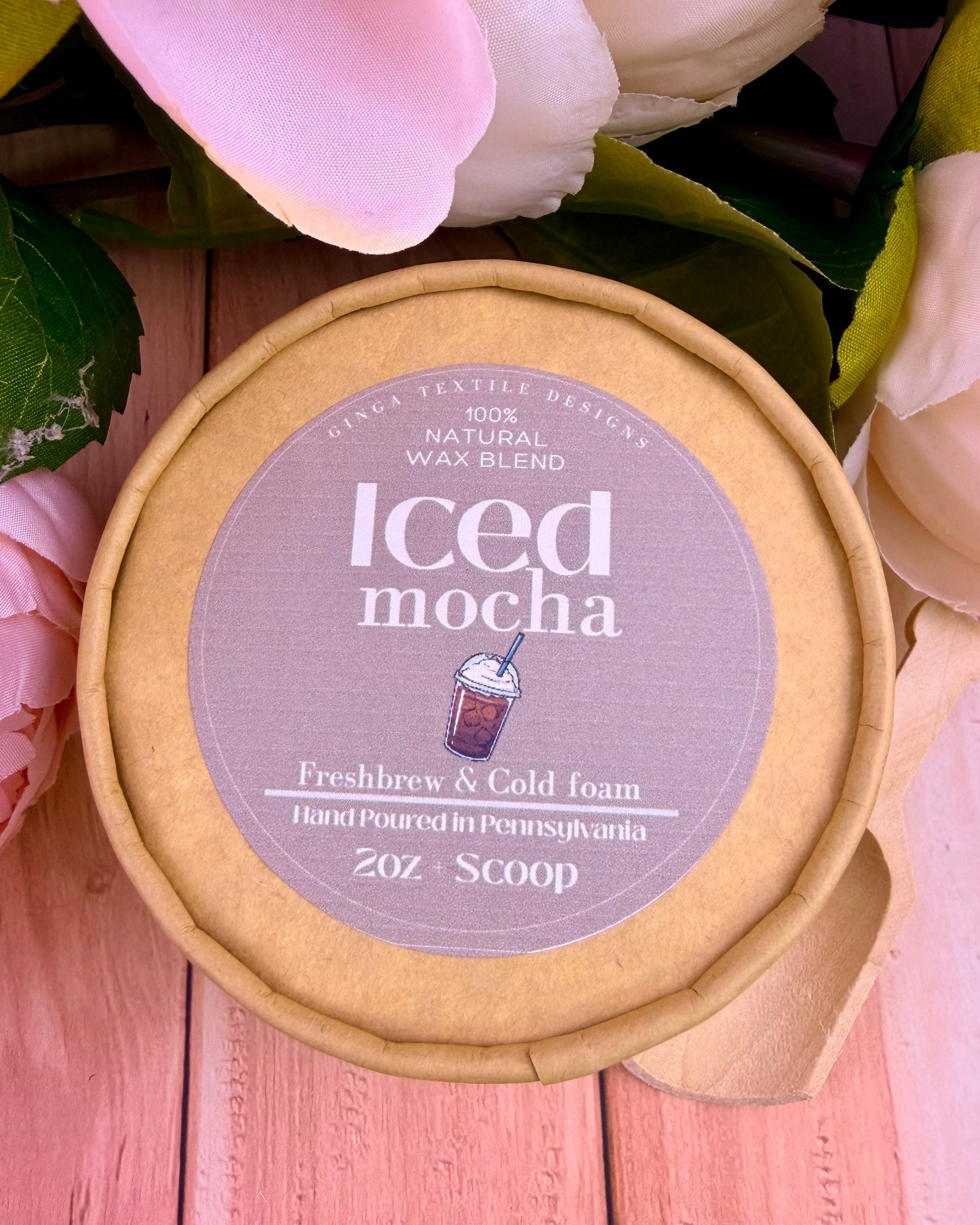 Overview of a packaging for a wax melt scent of iced mocha on a light-colored wood table and flowers in the background.