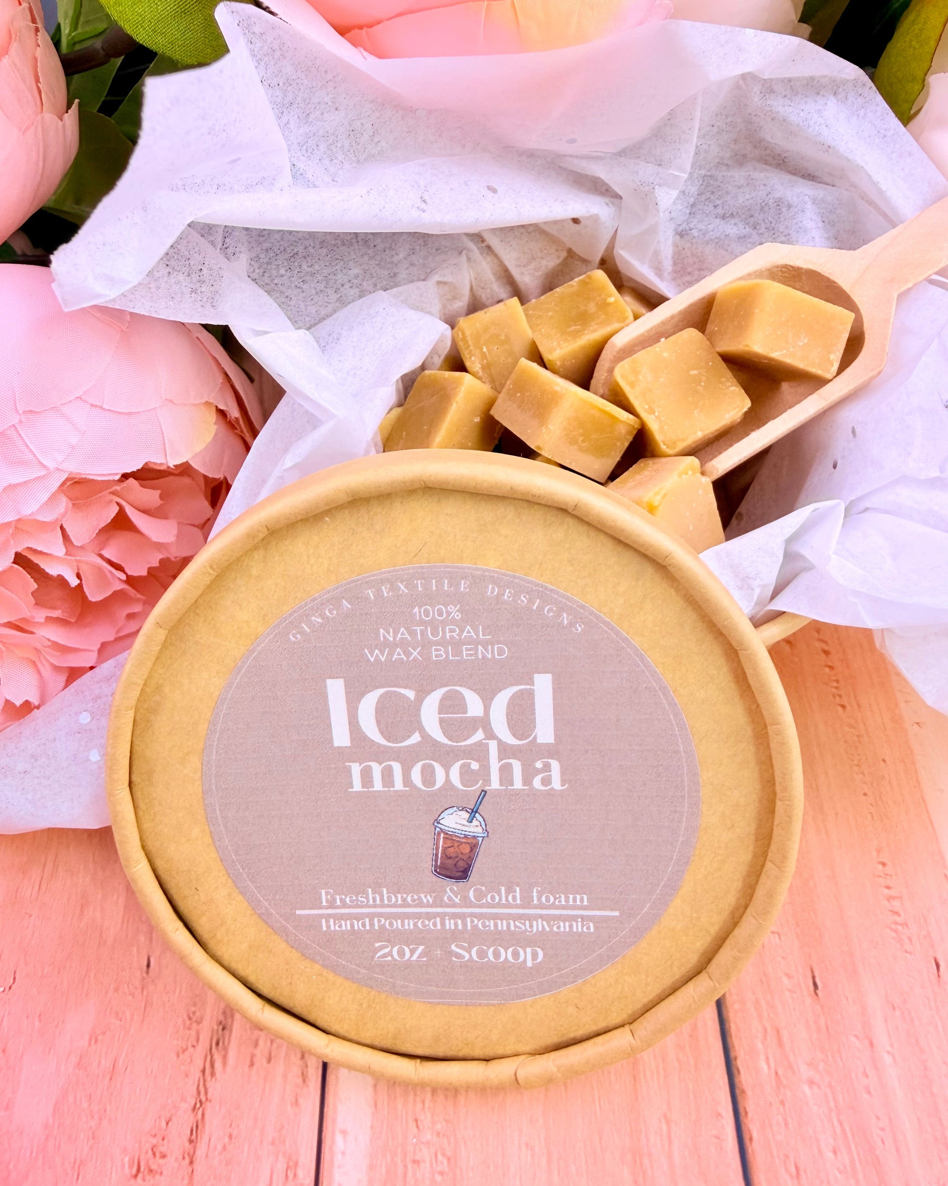 Wax melt scent packaging on a light-colored table and flowers in the background the scent is Iced mocha.