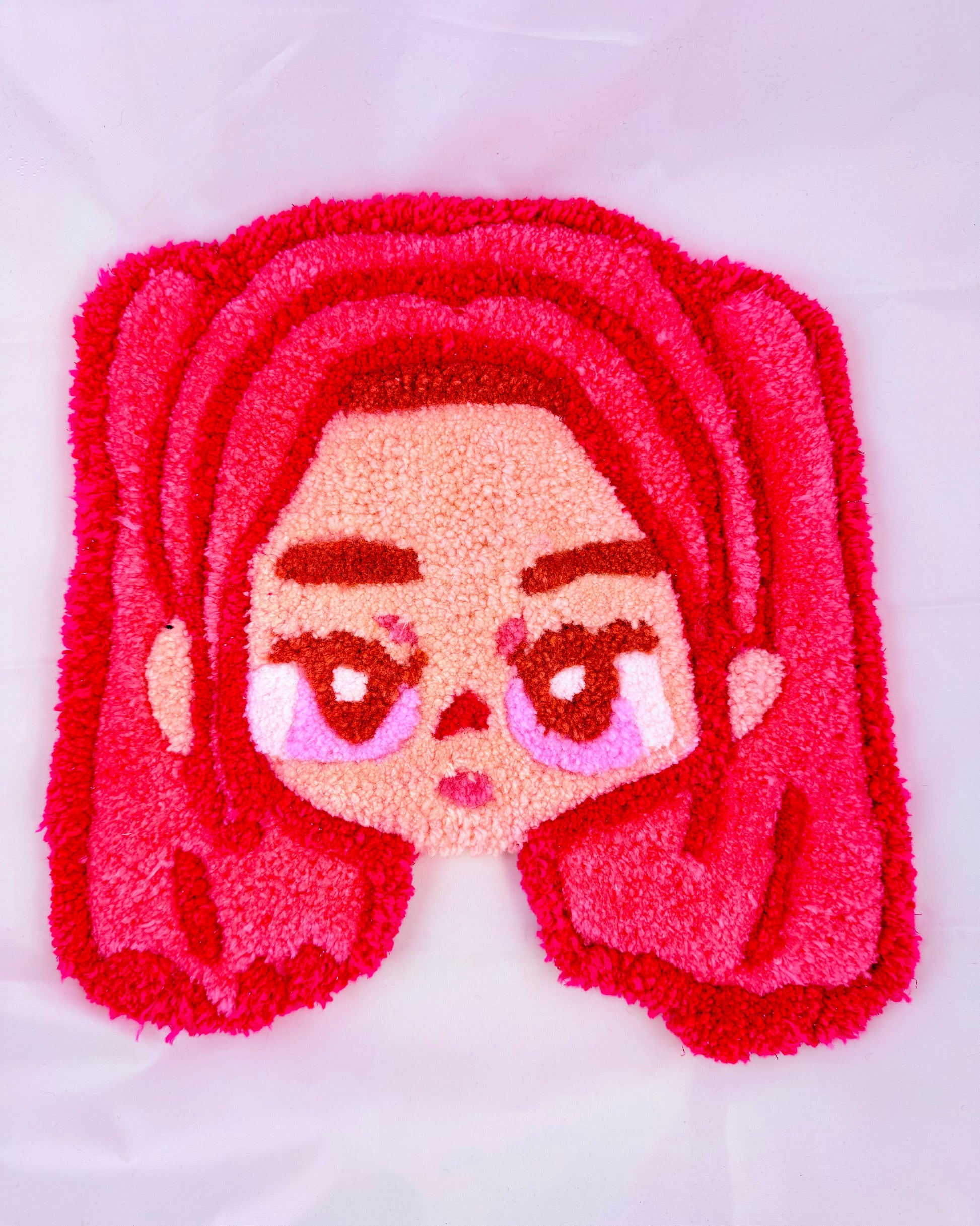 Tufted rug with cartoon character face featuring pink hair and eyes on a white background