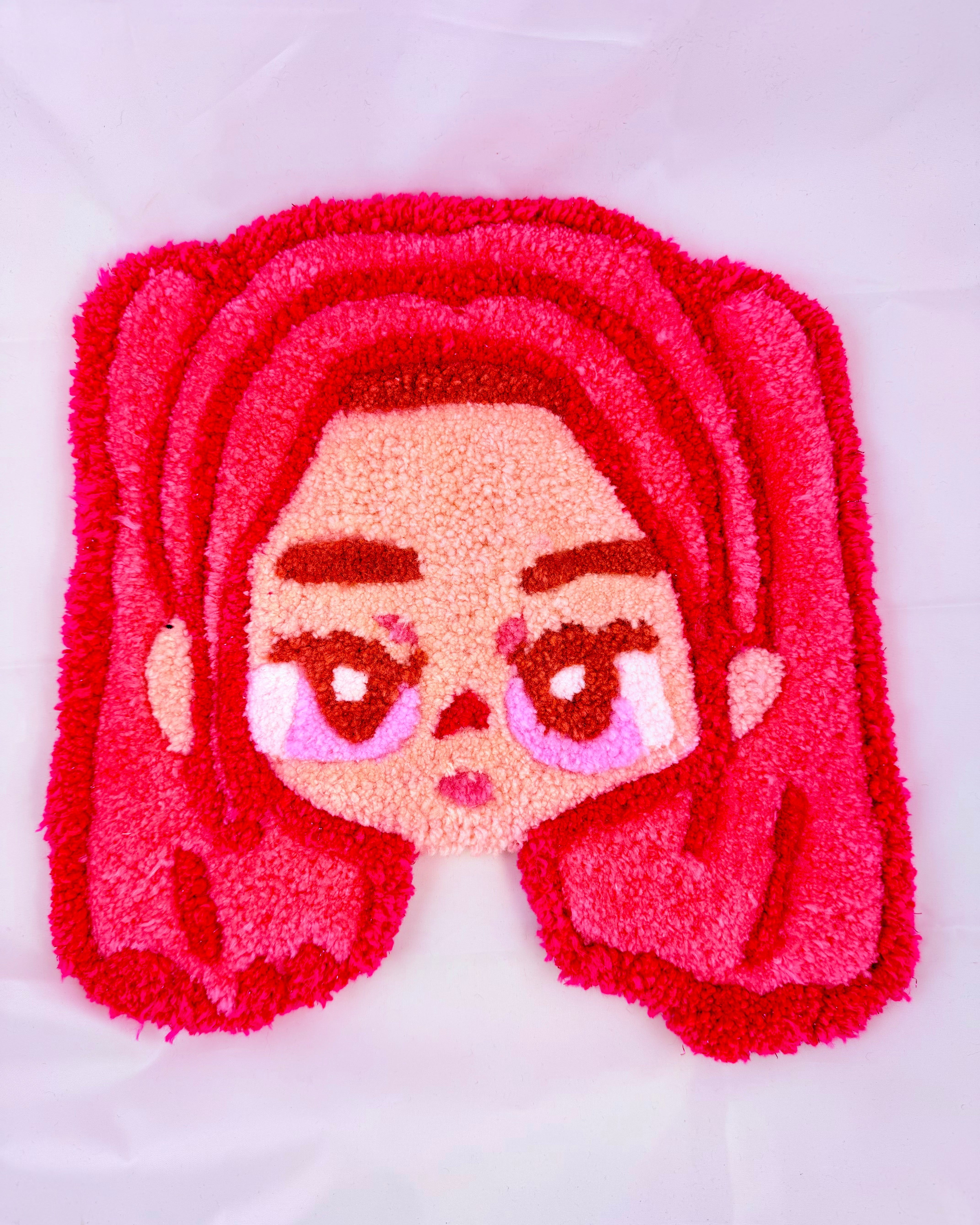 Tufted rug with cartoon character face featuring pink hair and eyes on a white background