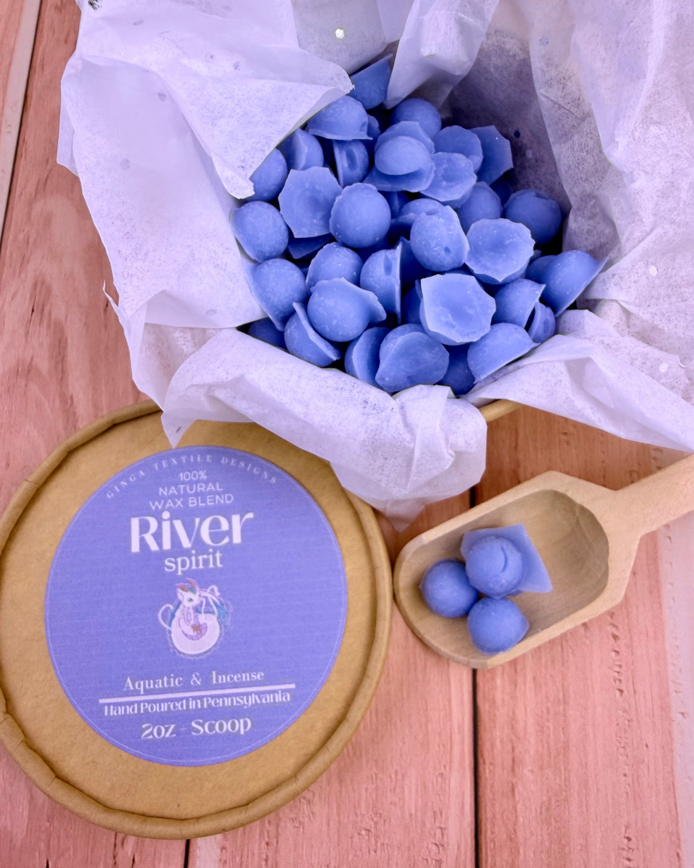 Blue wax melts in a bowl with a lid labeled 'River Spirit' on a wooden surface.