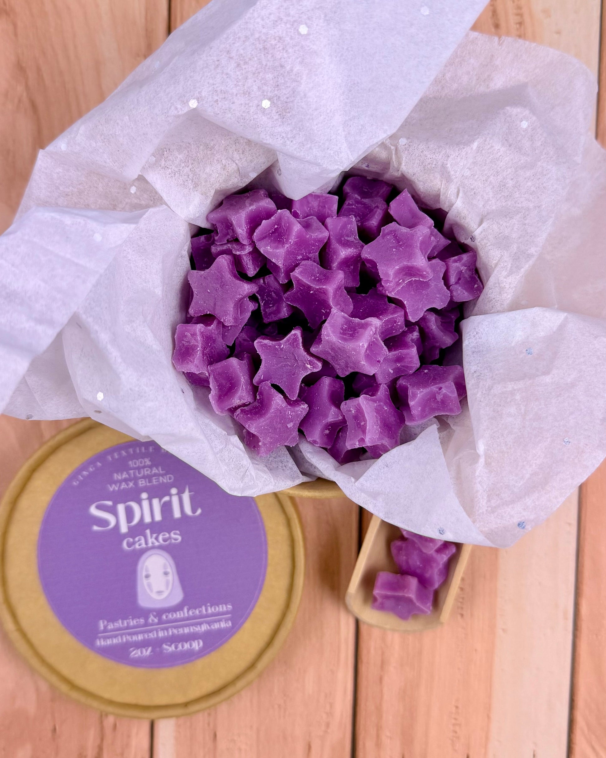 Purple star-shaped wax melts in a cardboard with a 'Spirit Cakes' container on a wooden surface.