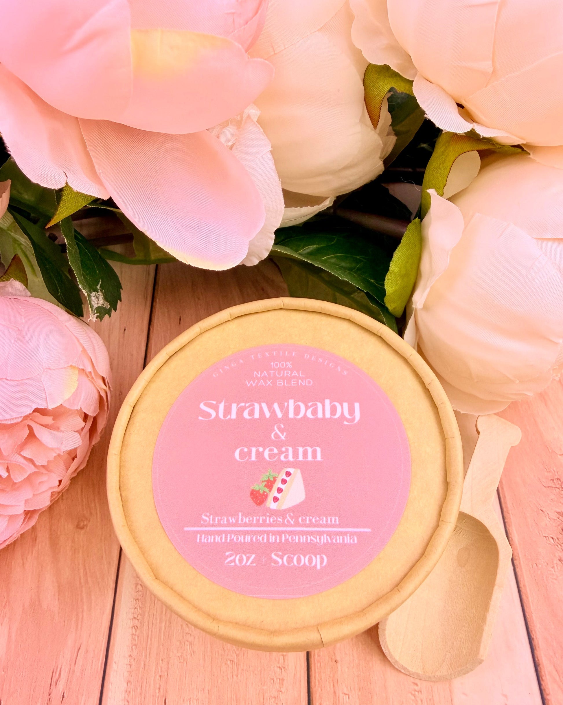 Strawberry & Cream wax melts with pink label surrounded by pink flowers on a wooden surface
