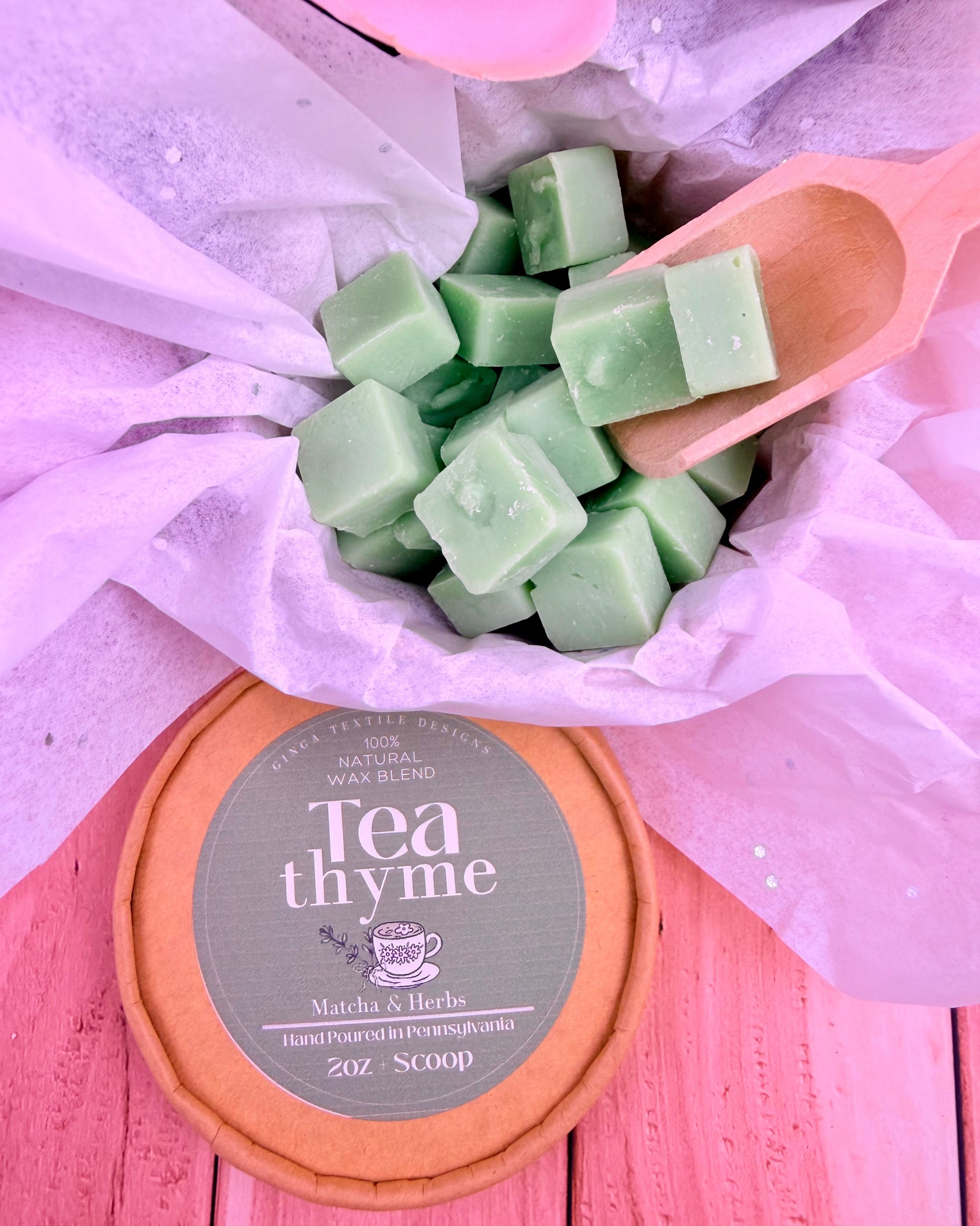 Green wax melts in a pink scoop on a pink surface with 'Tea Thyme' packaging.