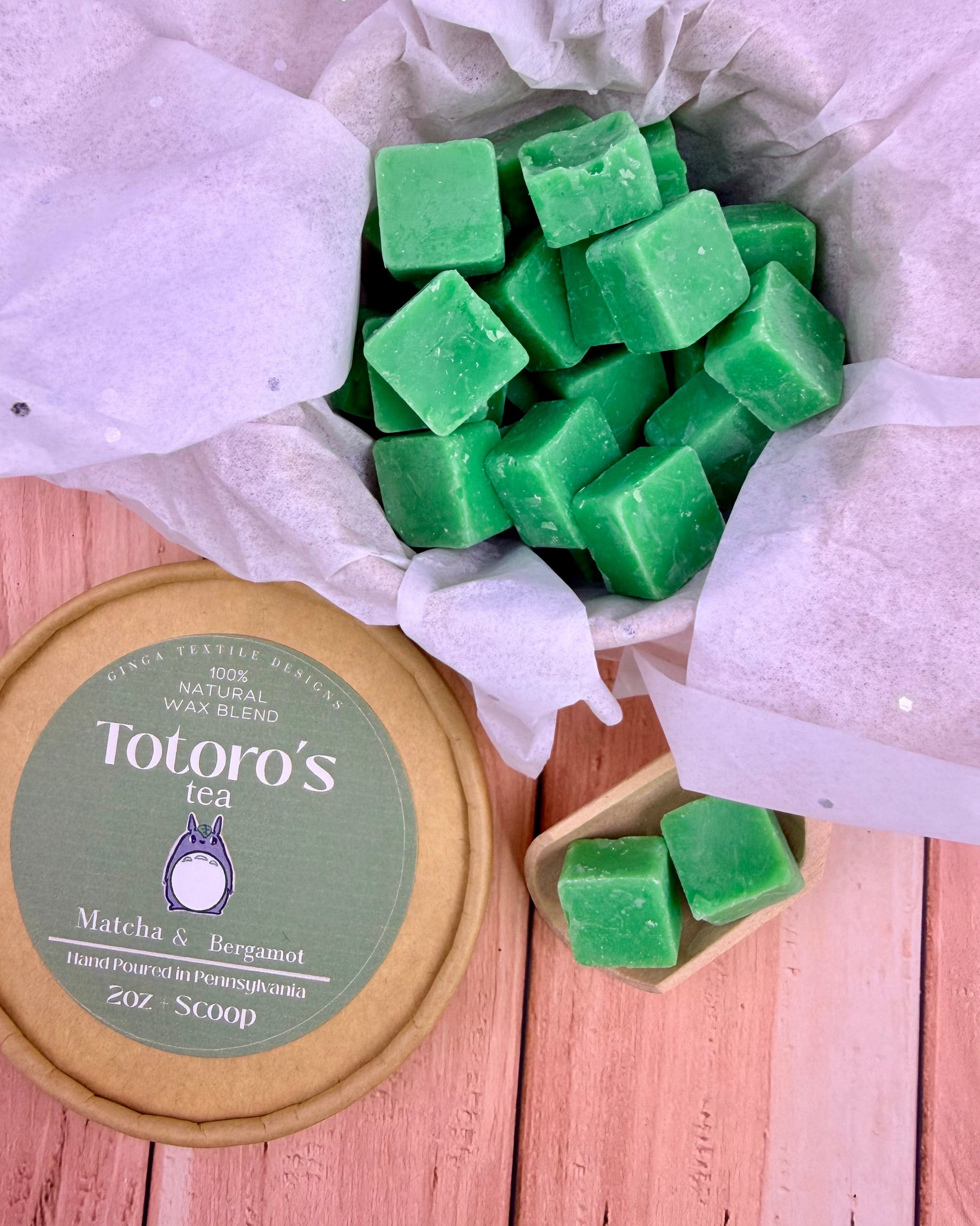 Green wax cubes in a container with a Totoro's Tea packaging on a wooden surface.