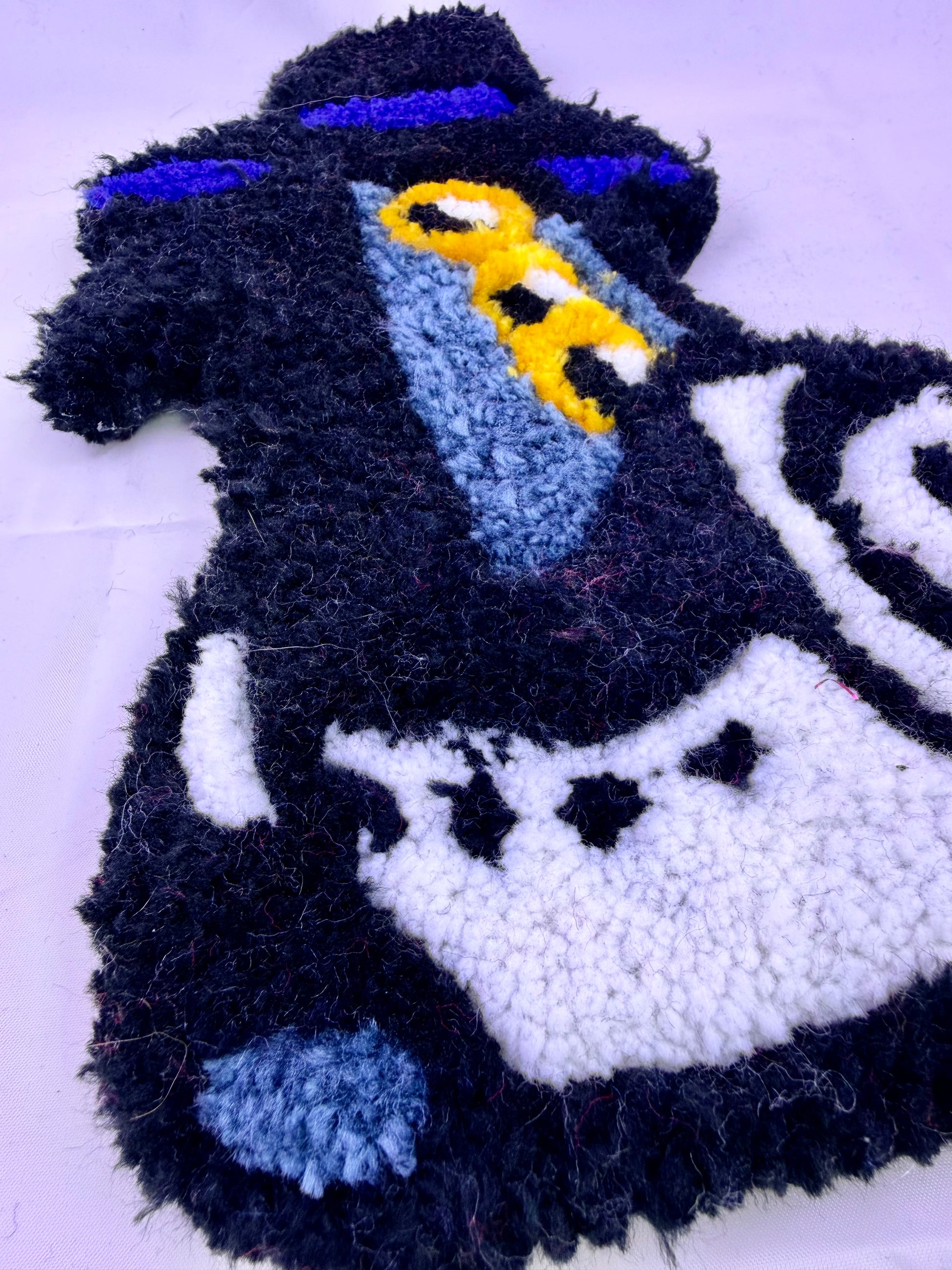 Textile tufted of a magpie sussie wearing a hat and scarf on a white background
