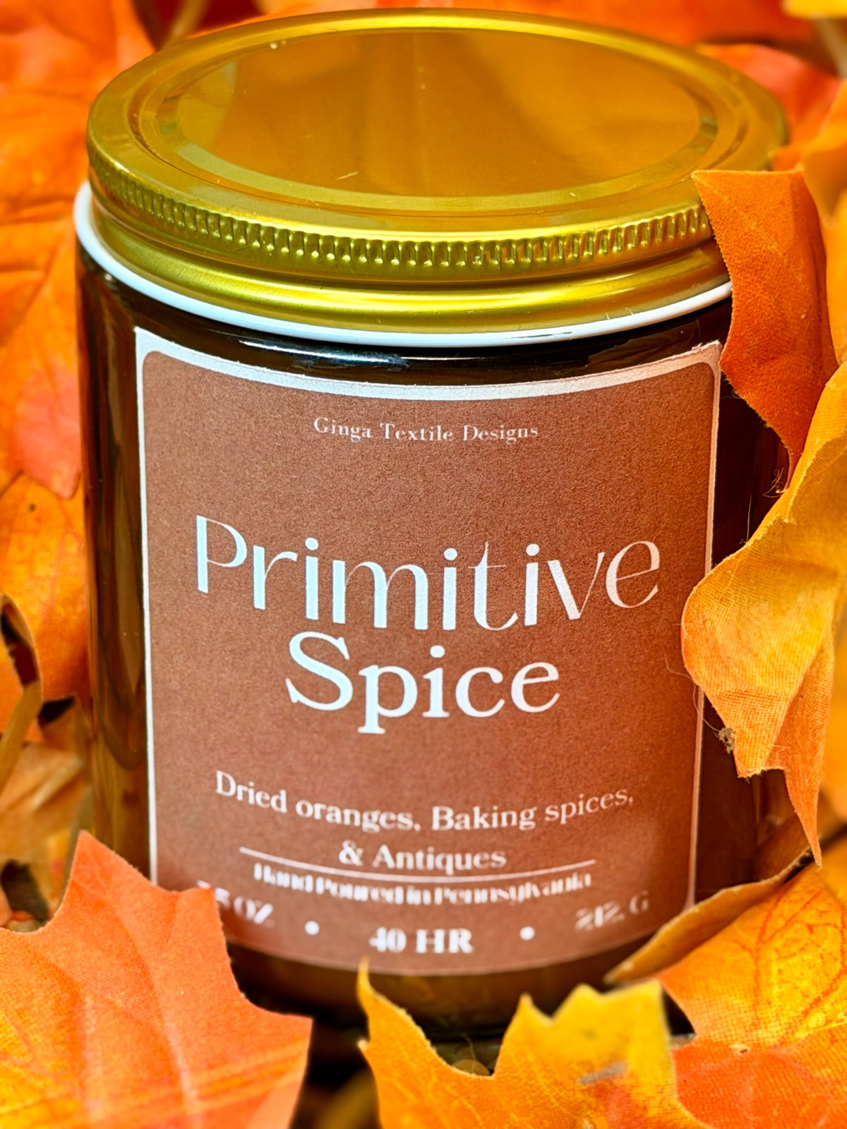 Primitive Spice 7.5 oz amber glass candle with gold lid styled with autumn leaves